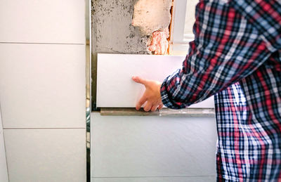 Detail of hand of unrecognizable female bricklayer laying tile on the wall in bathroom renovation