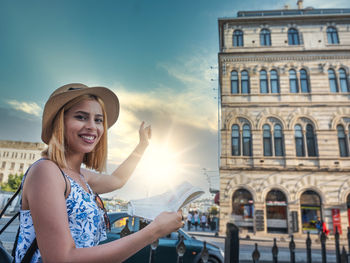 Portrait of smiling woman holding building in city against sky