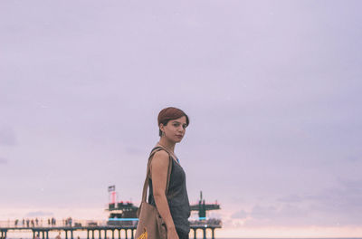 Portrait of woman standing by railing against sky