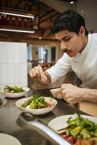 Focused male chef sprinkling salt on salad at commercial kitchen