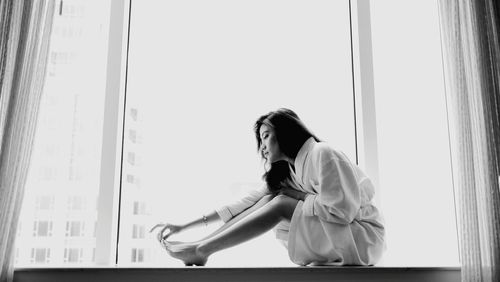 Side view of young woman sitting by window