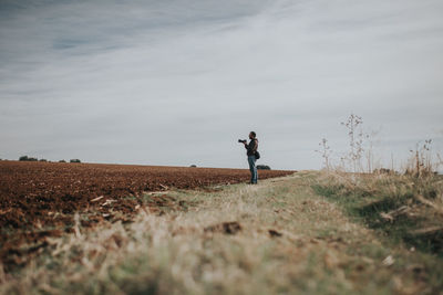 Side view of man photographing while standing at farm against sky