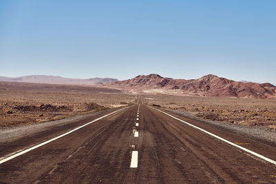 Road leading towards mountains against clear sky