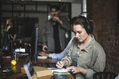 Businesswoman writing in note pad while working in office