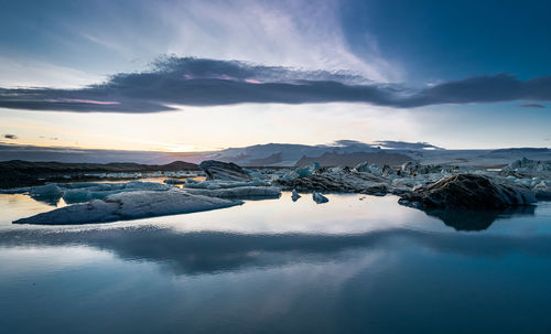 Scenic view of lake by snowcapped mountains against sky during sunset