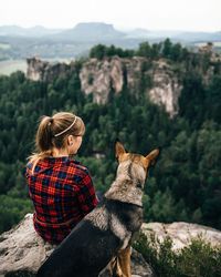 Rear view of woman sitting with dog at mountain peak