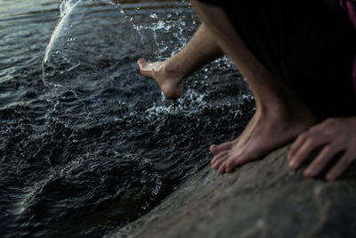 Low section of person crouching on rock by sea during sunset