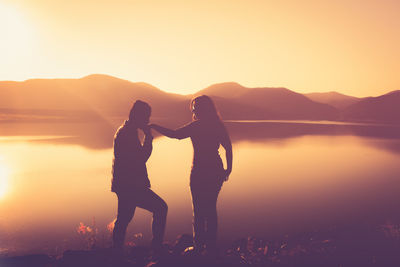 Silhouette couple standing on mountain against sky during sunset