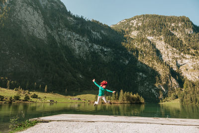 Happy woman jumping on pier against mountain