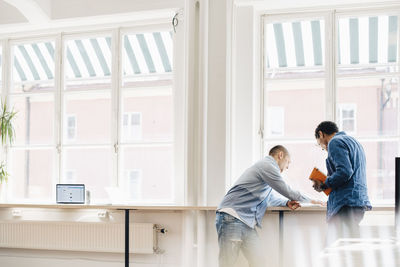 Male computer programmers discussing at desk by window in office