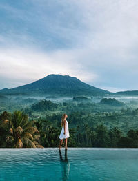 Rear view of woman standing in swimming pool against sky