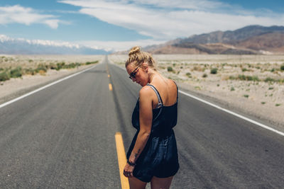 Rear view of young woman walking on road against sky