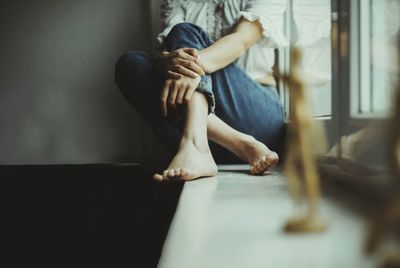 Low section of woman sitting on window sill at home