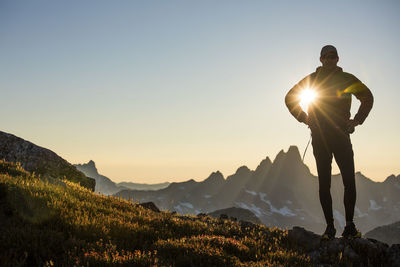 Sun shines through arm of silhouetted hiker on mountain ridge