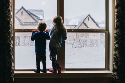 Rear view of siblings looking through window