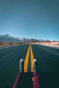 Low section of man sitting on country road against clear blue sky