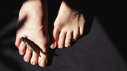 Low section of woman with artificial insect on foot over black background