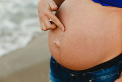 Midsection of pregnant woman standing at beach