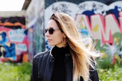 Beautiful young woman wearing sunglasses against graffiti wall