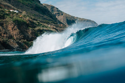 Scenic view of waves splashing in sea against mountain