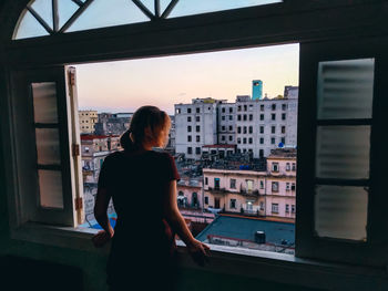 Rear view of woman looking through window at home