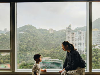 Mother talking with son while sitting on window sill at home