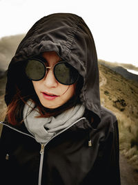 Portrait of young woman wearing sunglasses against sky during winter