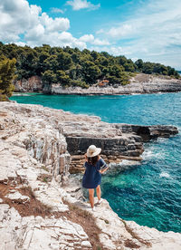 Young woman in summer outfit on cliff above sea.