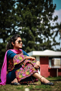 Full length of smiling woman sitting against trees