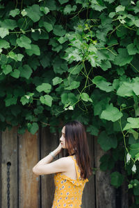 Beautiful woman standing by wooden wall against tree