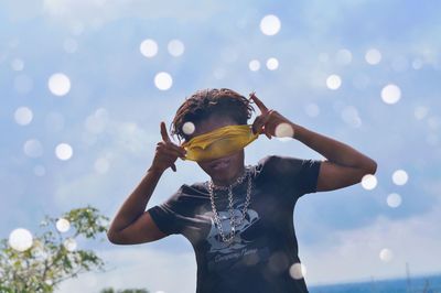 Portrait of woman covering eyes while standing against sky