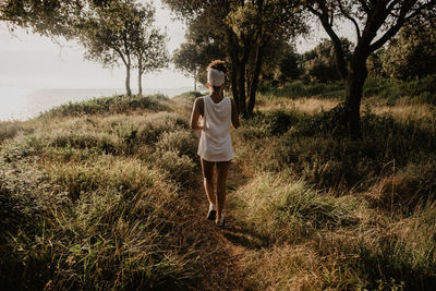 Rear view of woman walking on grassy field during sunset