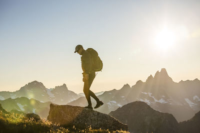 Back lit backpacker standing on mountain summit with scenic view