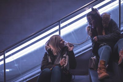 Female friends eating food while sitting on escalator