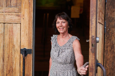 Portrait of smiling senior woman opening door of language school