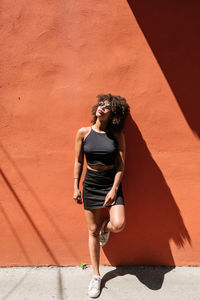 Young woman standing against wall during sunny day