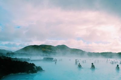 Crowd bathing in hot spring against cloudy sky