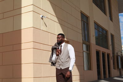 Young man looking away while standing against building