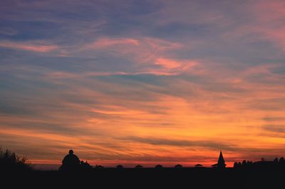 Silhouette of buildings against cloudy sky during sunset