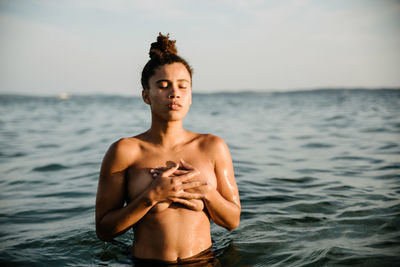 Shirtless young woman swimming in sea against sky