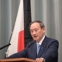 記者会見で質問に答える菅義偉官房長官。奥は東日本大震災の犠牲者を哀悼の意をあらわす弔旗＝首相官邸で2020年3月11日午前11時21分、川田雅浩撮影