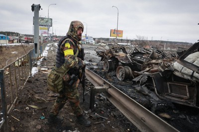 ロシア軍の車両の残骸近くに立つ武装した男性＝ウクライナの首都キエフ近郊で2022年3月1日、AP