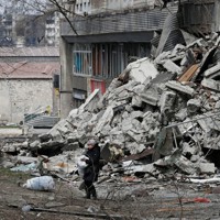 ウクライナとロシアの紛争で破壊された集合住宅の近くで袋を運ぶ地元住民＝ウクライナ・マリウポリで2022年3月31日、ロイター