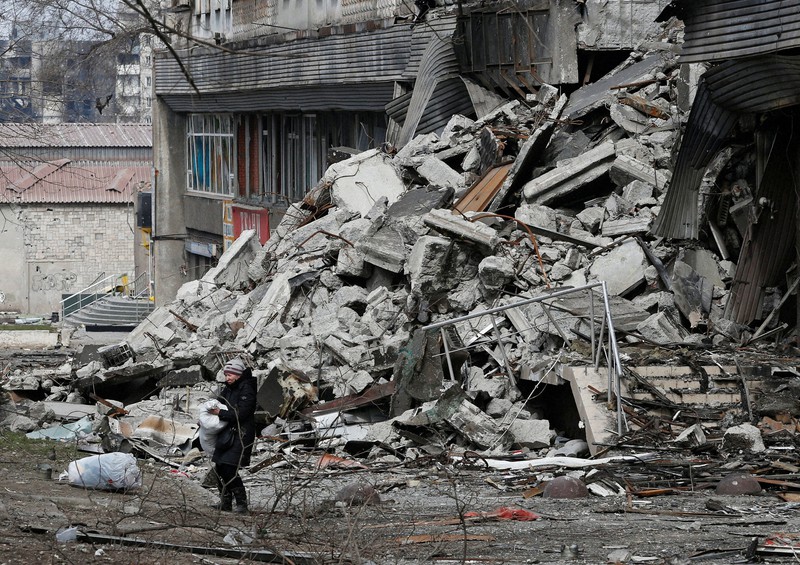 ウクライナとロシアの紛争で破壊された集合住宅の近くで袋を運ぶ地元住民＝ウクライナ・マリウポリで2022年3月31日、ロイター