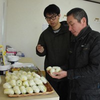 出勤前に訪れた利用者に、おむすびの種類を説明する北村優斗さん（左）＝石川県輪島市河井町で2024年3月15日午前7時33分、古川幸奈撮影