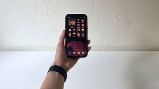 A person's hand holding an iPhone showing the home screen in iOS 18