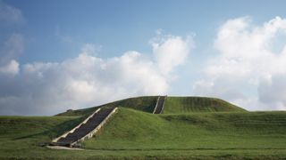 Staircase up grass hilltop with puffy clouds in sky