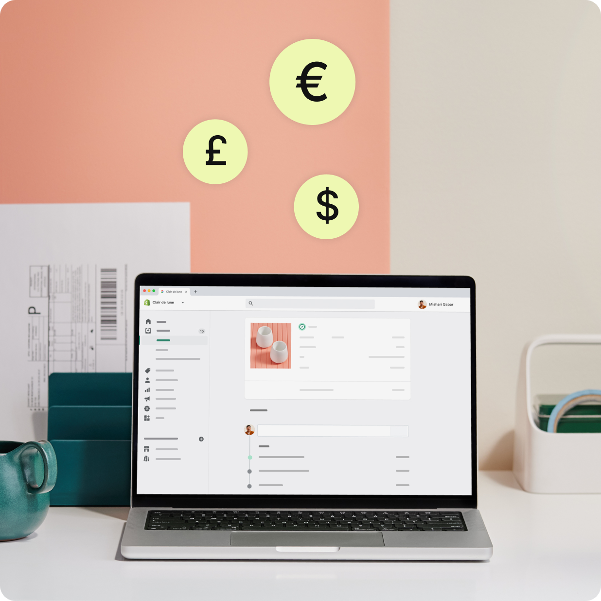 주문과 인보이스가 표시된 Shopify Payments 화면을 띄워 둔 노트북과 다양한 통화 기호