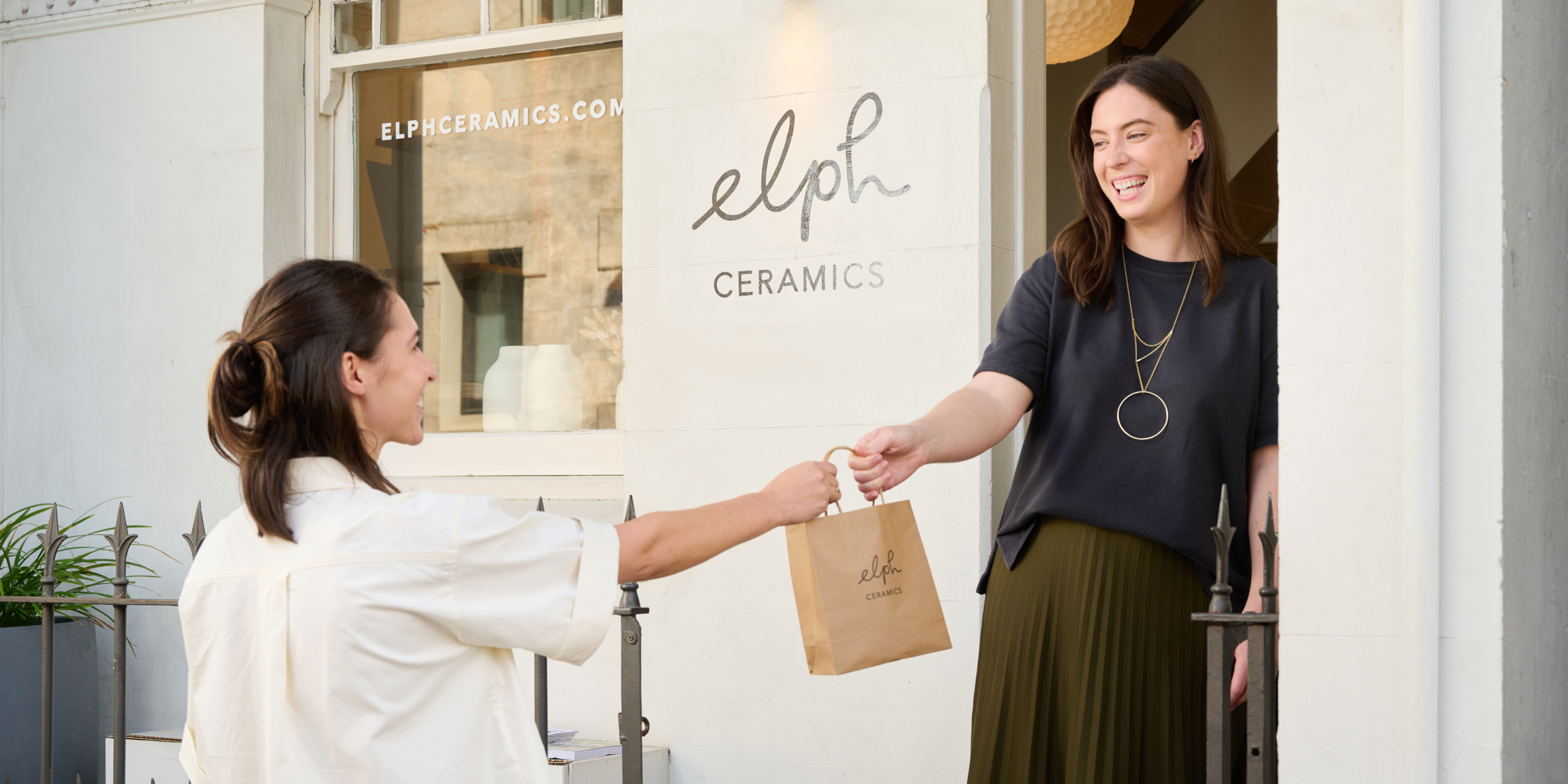 Two sales associate serve customers at the counter using Shopify POS hardware. One uses the countertop system to checkout while the other processes an in-store pickup on POS Go.