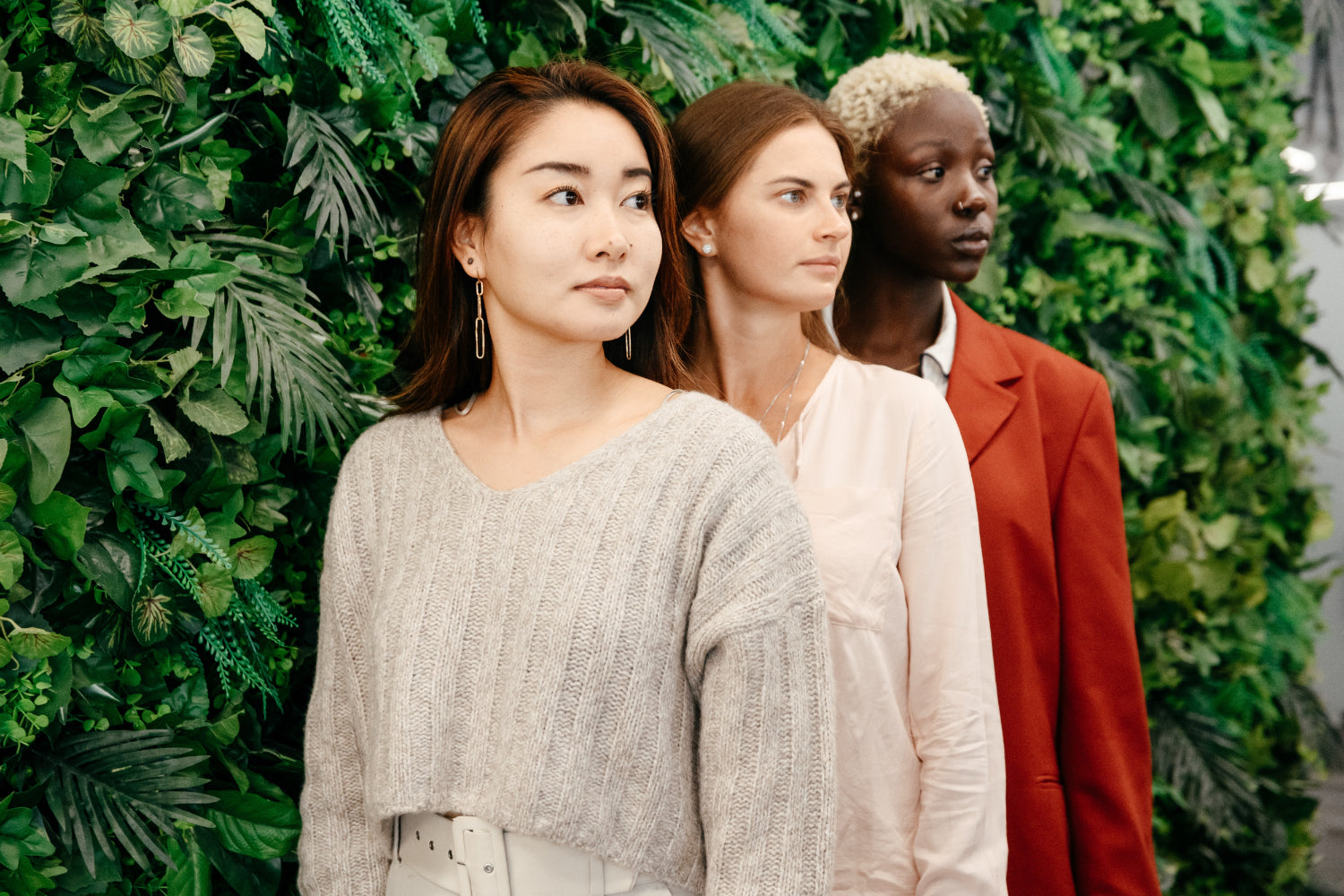 Three women stand front to back in front of a bush